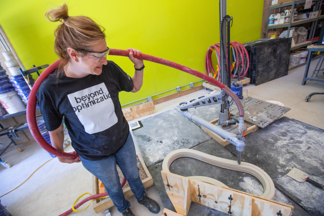 An Iowa State University professor holds a hose connected to the nozzle of a 3D printer as it fabricates a concrete structure